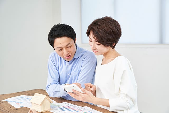 家の模型と電卓で計算する夫婦