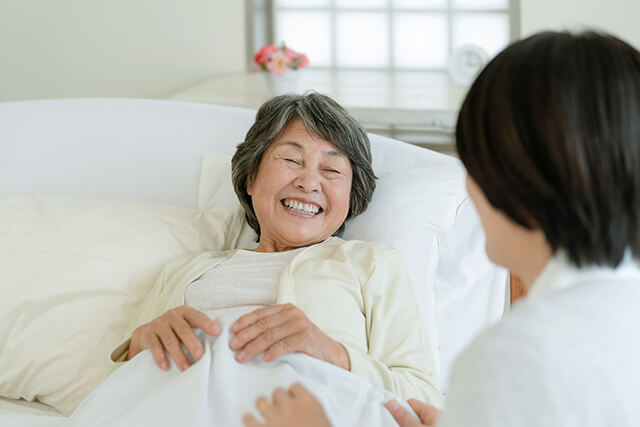 介護ベッドで寝るシニア女性と介護者