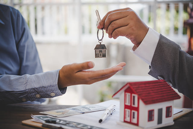 家の模型と鍵を渡す人の手