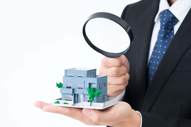 家の模型を虫眼鏡で見る男性