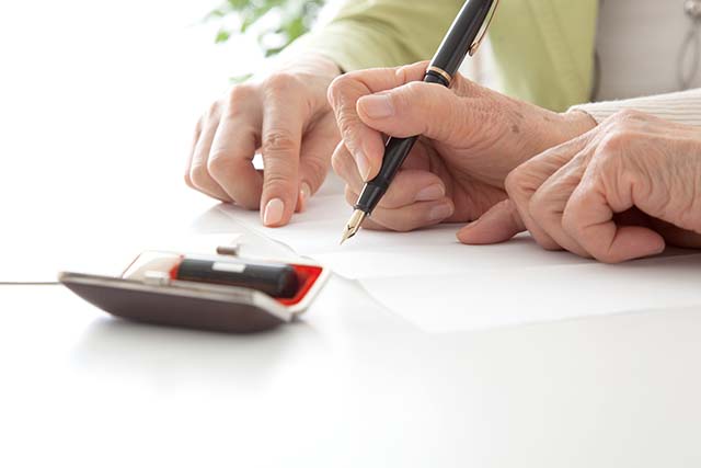 書類に記入するシニア夫婦の手元、印鑑