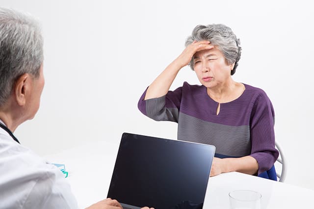 頭をかかえる高齢の女性とパソコンと医師