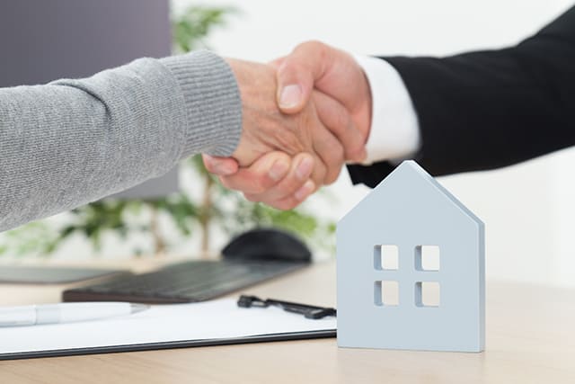 家の模型と握手する人の手