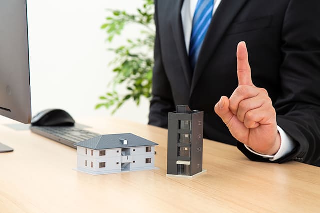 住宅模型と指を立てている人
