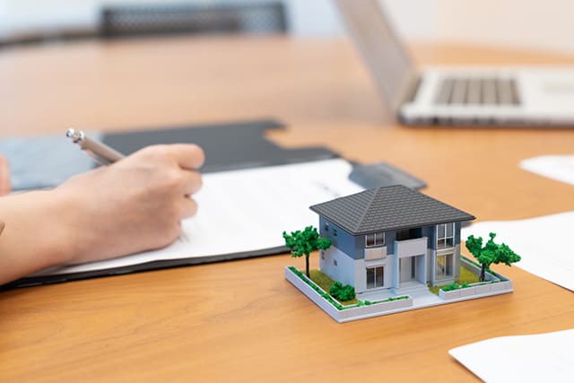 家の模型と契約書にサインする人