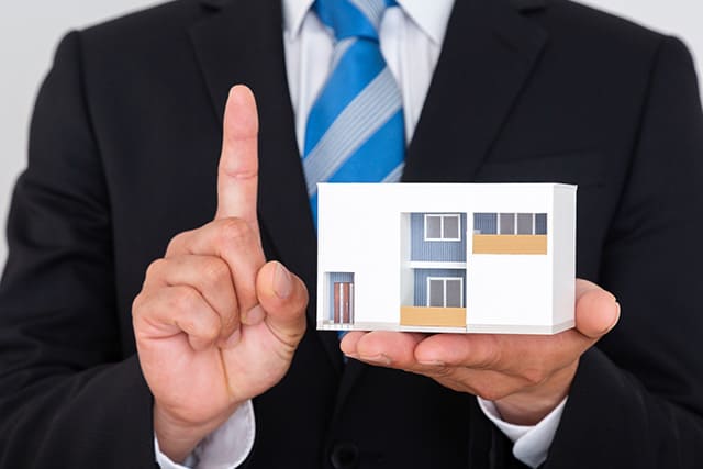 人が人差し指を立てている様子 家の模型