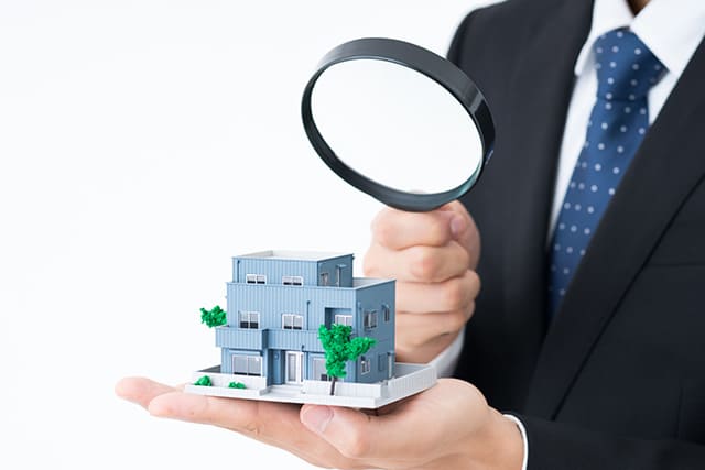 家の模型を虫眼鏡で見る男性