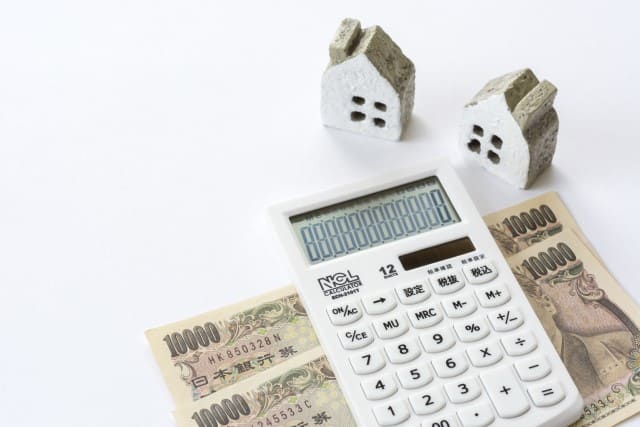 2つの家の模型と電卓と紙幣